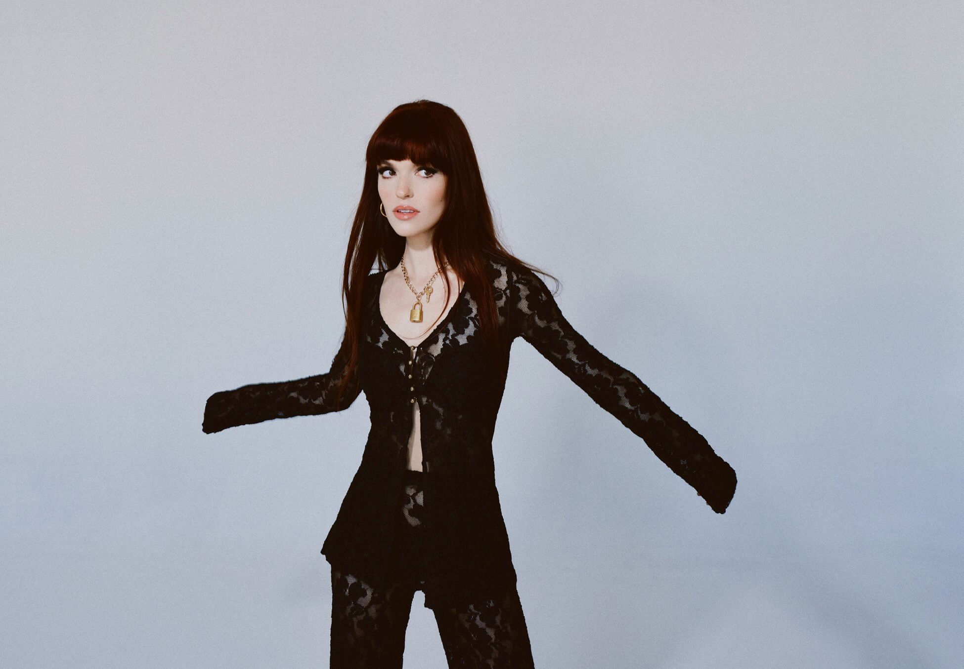 Lily Kinade stands in front of a gray backdrop wearing a black lace outfit