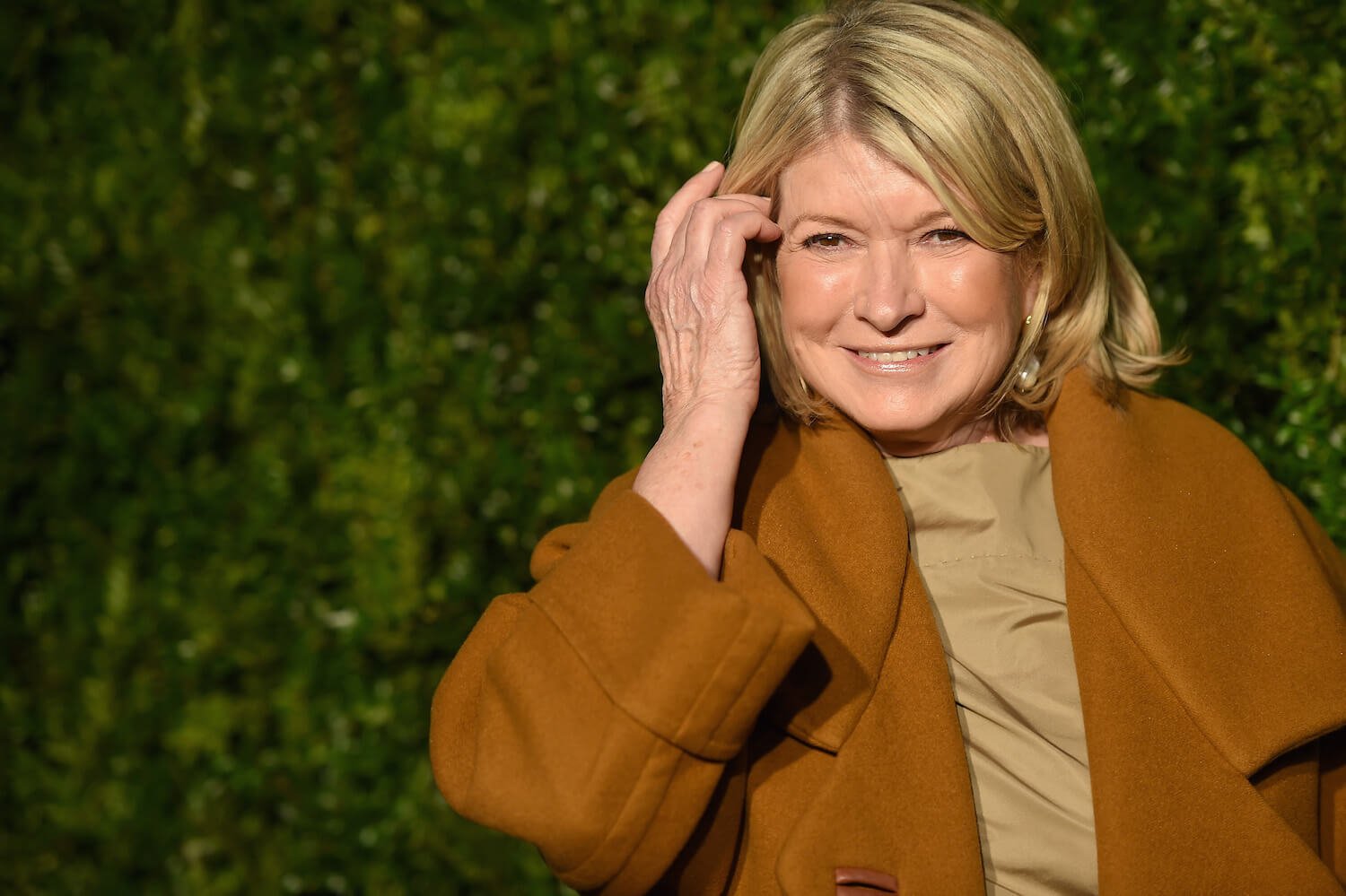 Martha Stewart smiling and tucking her hair behind her ear against a grassy background