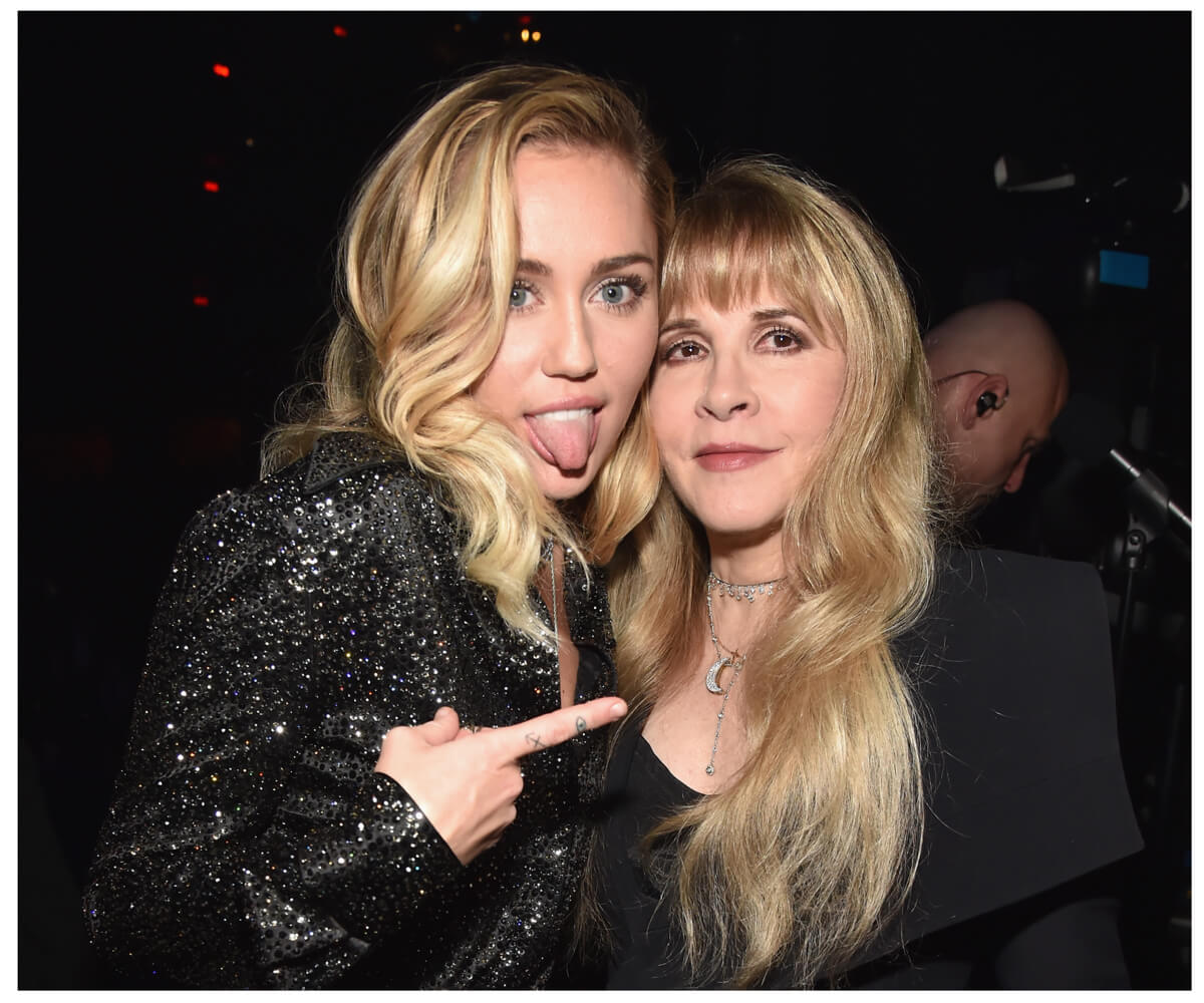 Miley Cyrus sticks her tongue out and points her finger at a smiling Stevie Nicks.