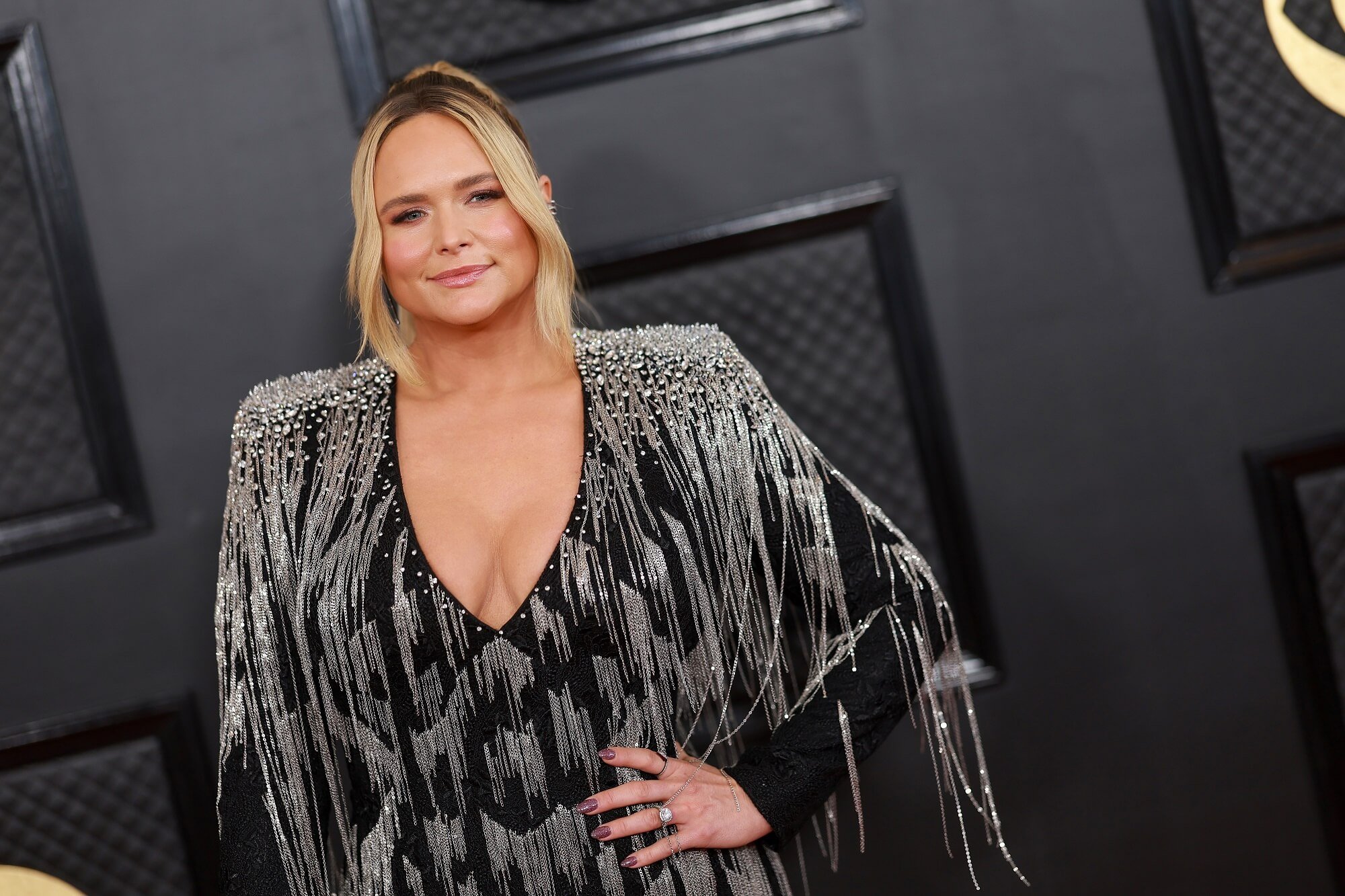 Miranda Lambert stands with her hand on her hip in front of a black wall