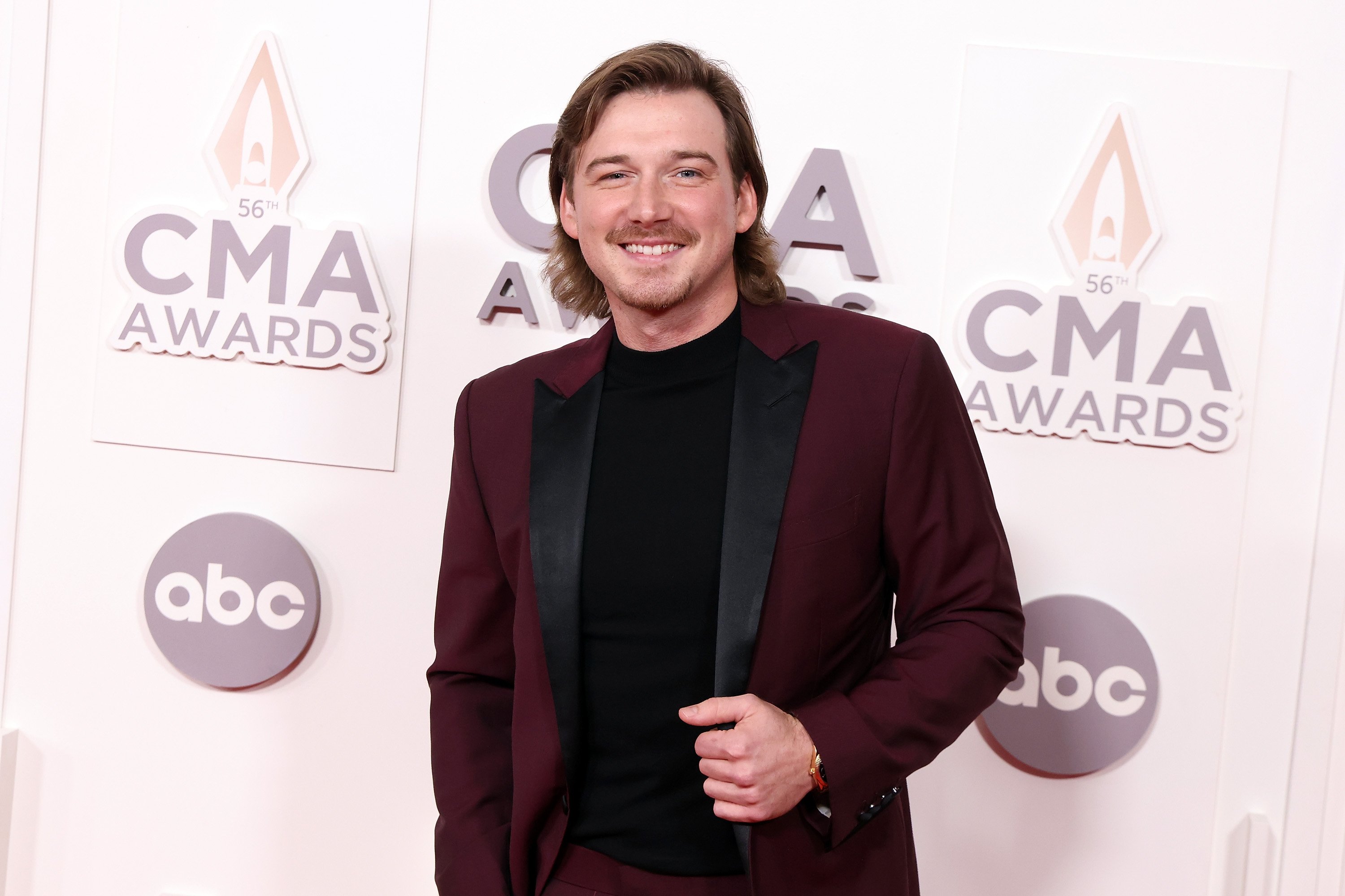 Morgan Wallen in a burgundy and black suit in front of a CMA Awards backdrop