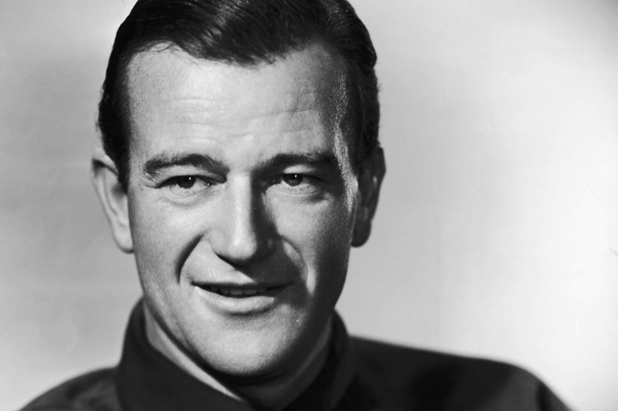 Movie star John Wayne in a black-and-white portrait with a smile on his face