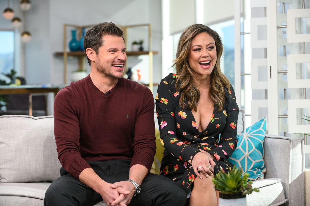 Nick Lachey and Vanessa Lachey sit on a couch smiling and laughing.