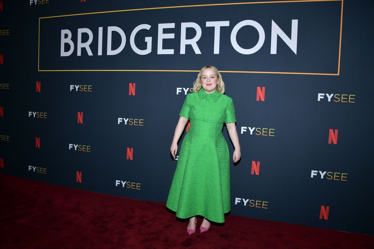 Nicola Coughlan poses in front of a black backdrop with the "Bridgerton" and Netflix logos.