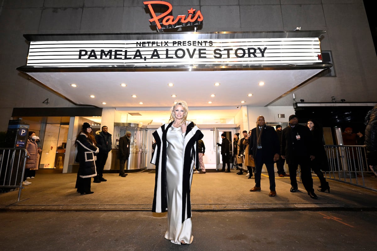 Pamela Anderson poses in front of a marquee with "Pamela a Love Story" on it.