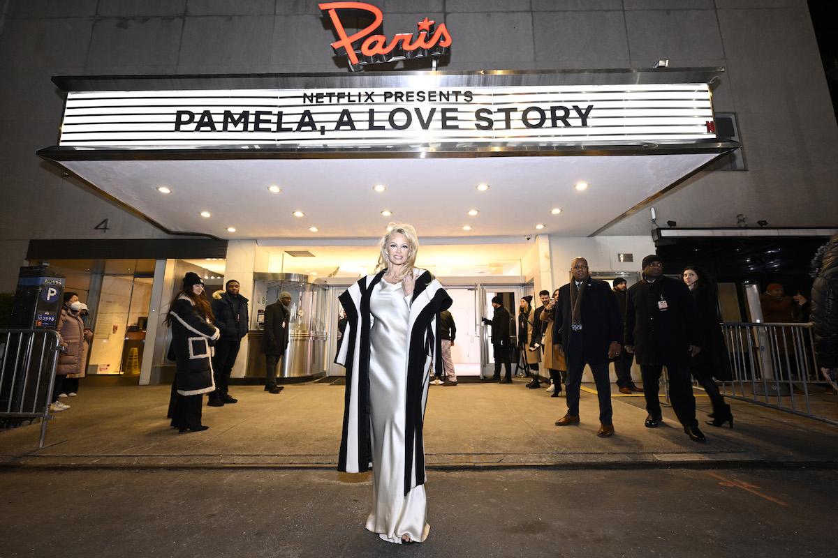 Pamela Anderson poses in front of a marquee with "Pamela a Love Story" on it.