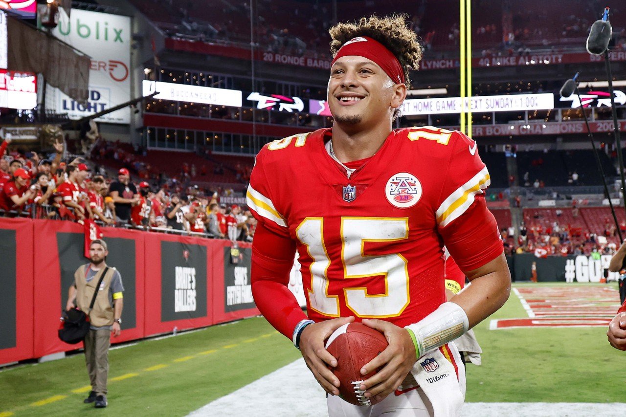 Patrick Mahomes smiles and holds a football.