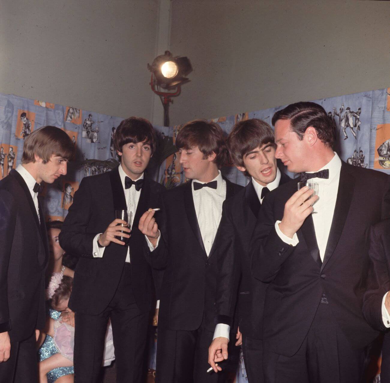 Ringo Starr, Paul McCartney, John Lennon, George Harrison, and Brian Epstein wears tuxedos and stand in a line. 