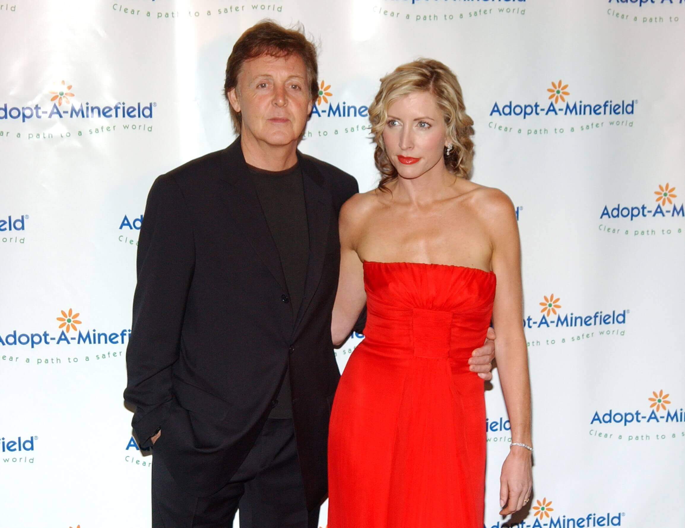 Paul McCartney and Heather Mills pose together. McCartney wears black and Mills wears a red dress.