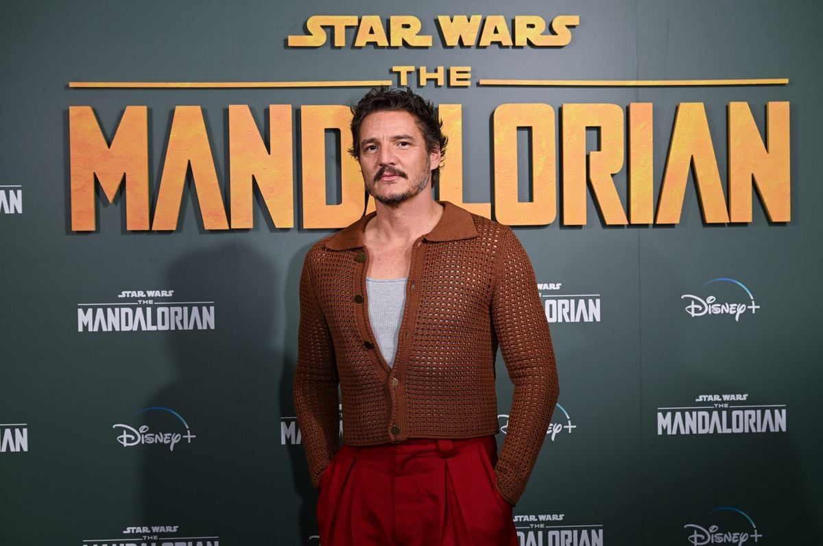Pedro Pascal poses in front of a backdrop with "The Mandalorian" logo.