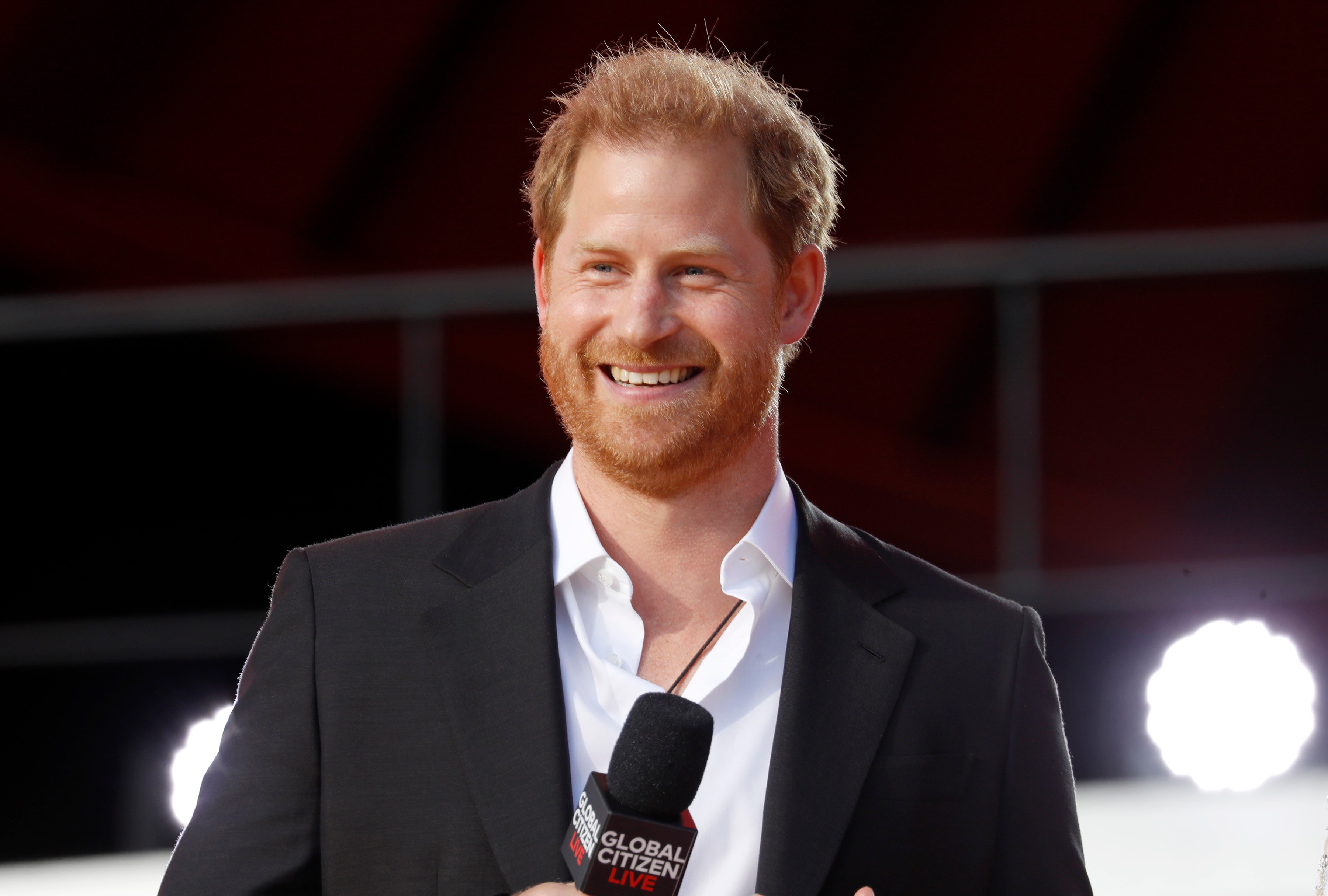 Prince Harry smiles while holding a microphone.