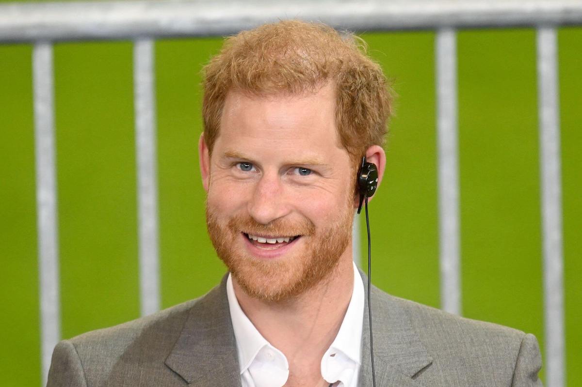 Prince Harry smiling, seated in front of a field