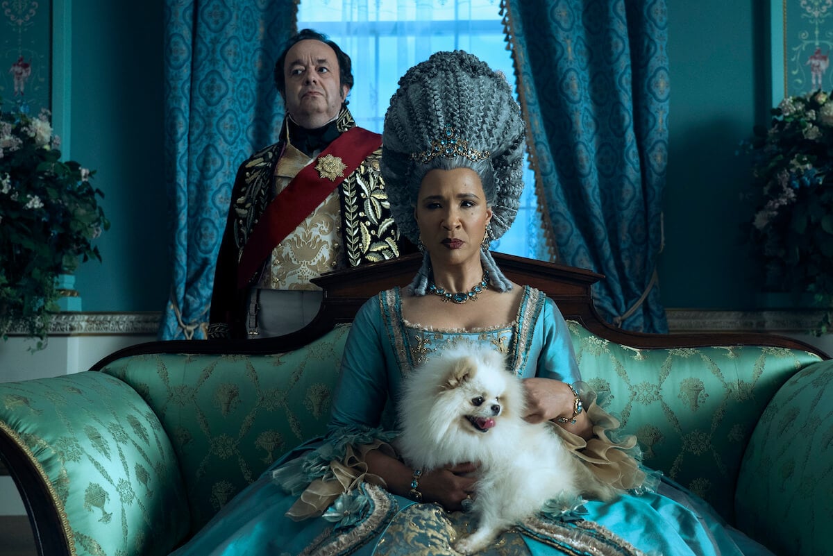 Golda Rosheuvel as Queen Charlotte holding a dog and sitting on her chair in ‘Queen Charlotte: A Bridgerton Story’