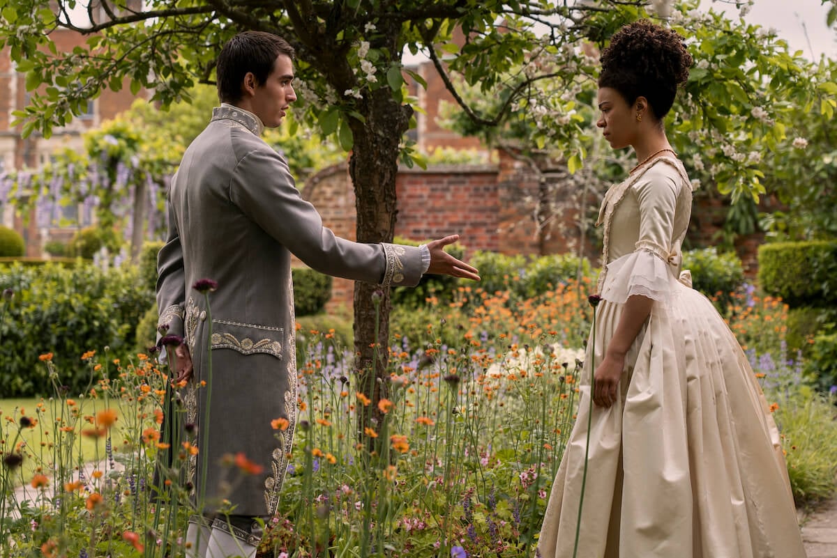 India Amarteifio as Queen Charlotte and King George as Corey Mylchreest greet each other in a garden in 'Bridgerton'
