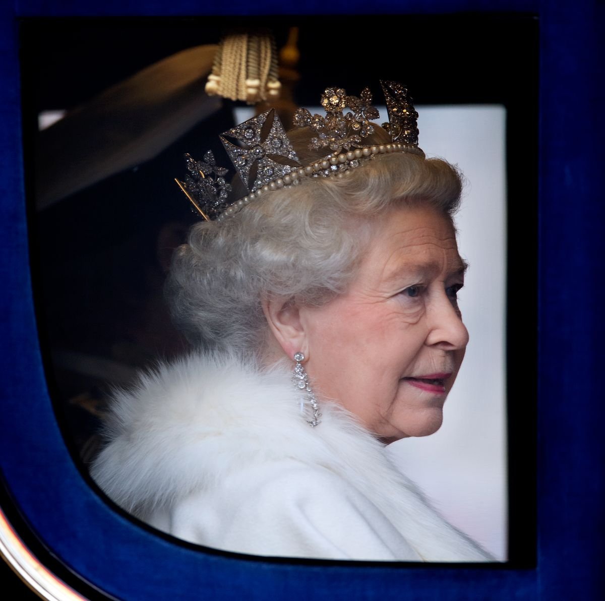 Queen Elizabeth II looks out the window while riding in a coach.