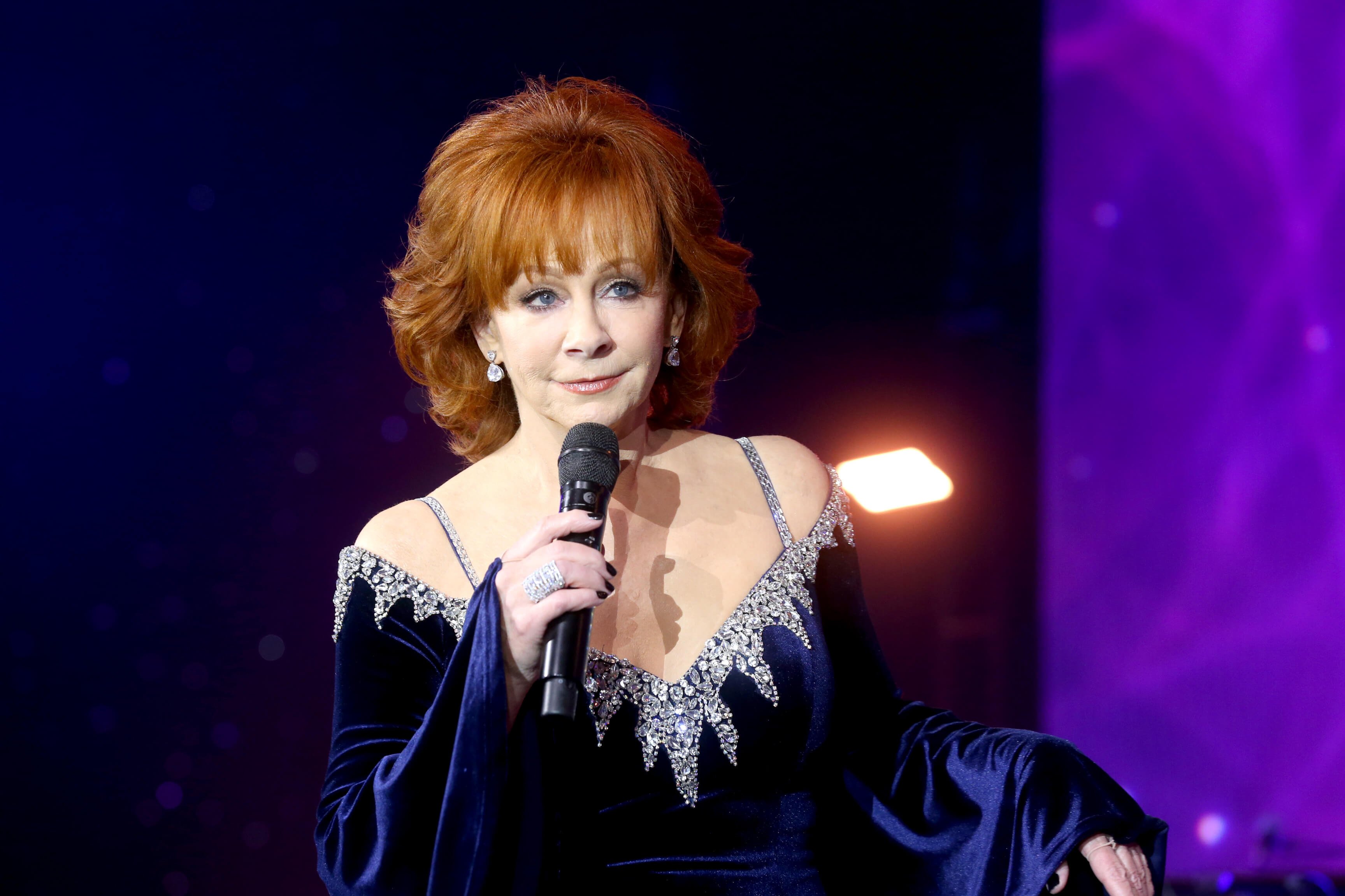 Reba McEntire holds a microphone while wearing a blue -and-silver strapless dress