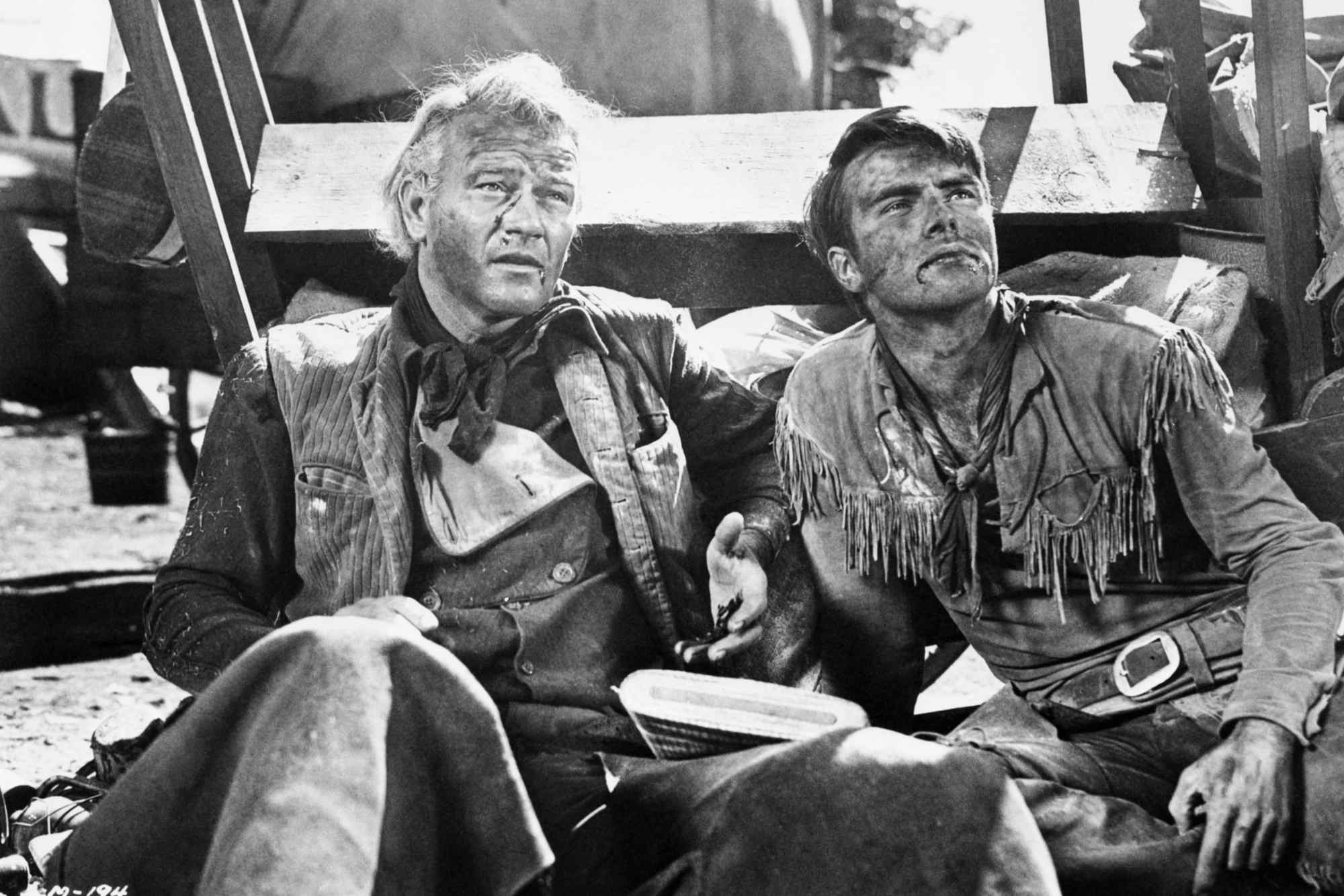 'Red River' John Wayne as Thomas Dunson and Montgomery Clift as Matt Garth sitting next to each other, covered in dirt