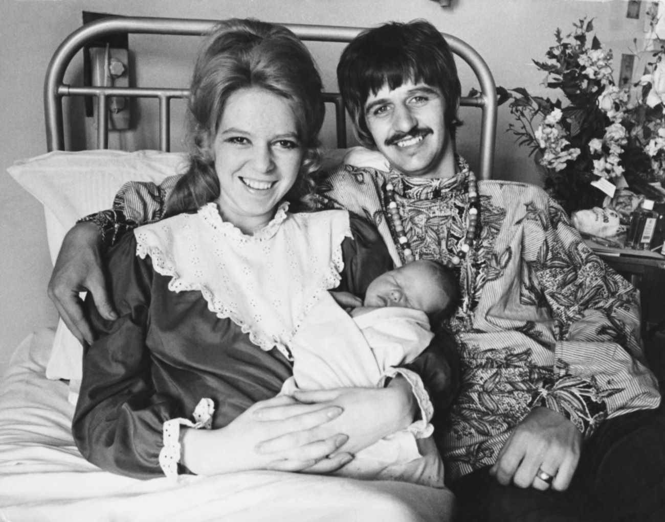 A black and white picture of Maureen Starkey and Ringo Starr sitting in a bed holding their infant son, Jason Starkey.