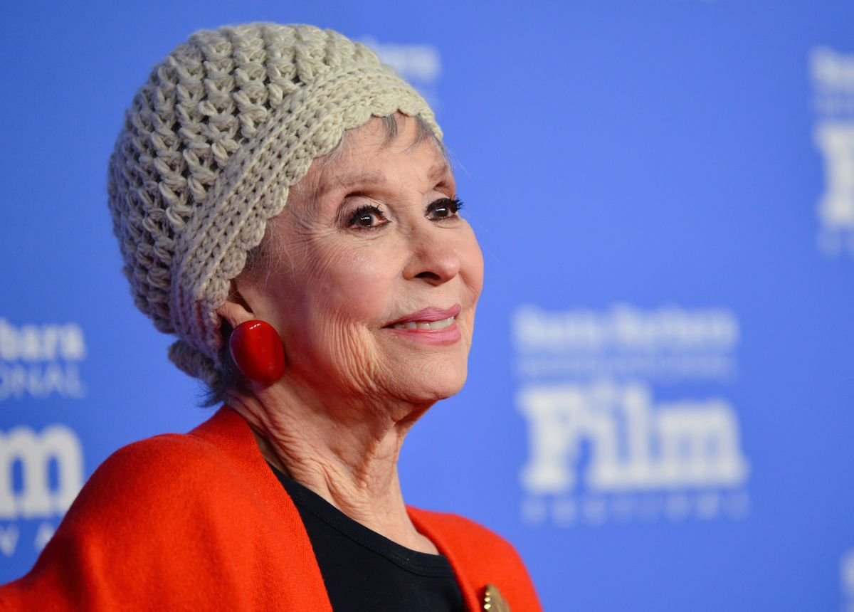 Rita Moreno poses in front of a blue backdrop