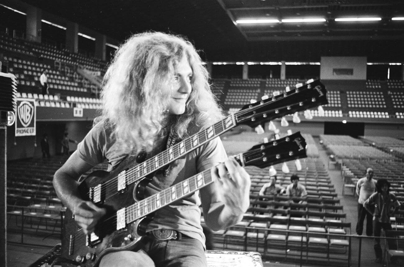 A black and white picture of Robert Plant holding a twin-necked guitar.