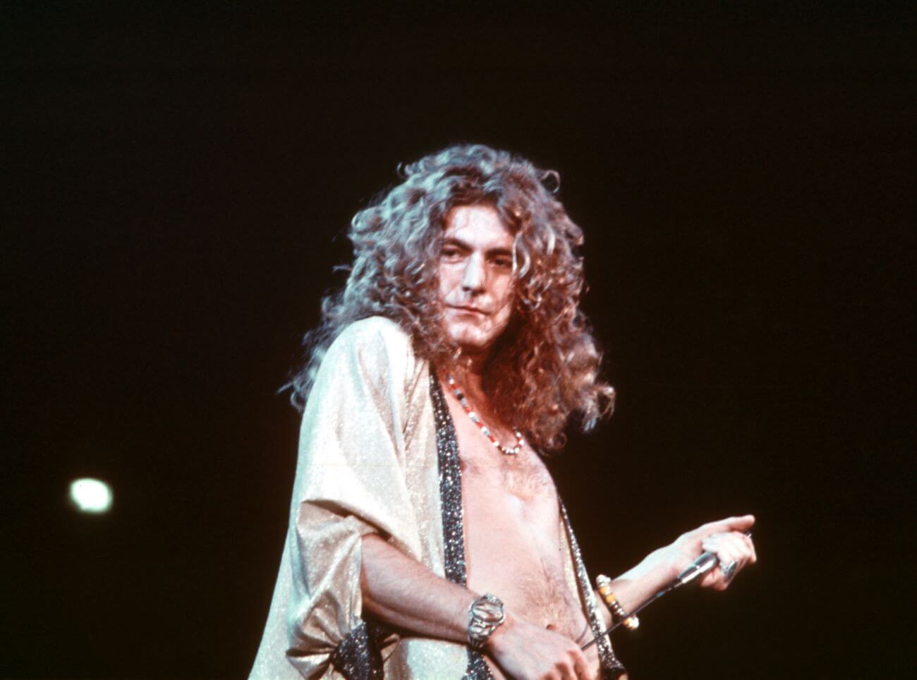 Robert Plant wears a necklace and holds a microphone.