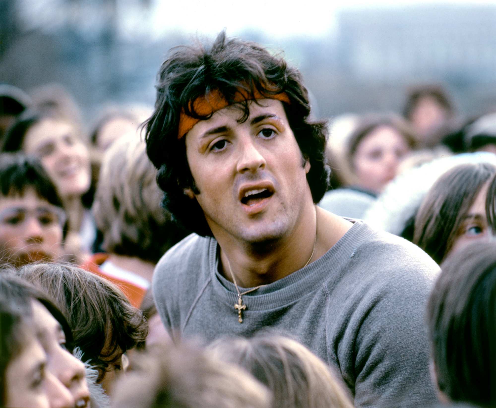 'Rocky II' Sylvester Stallone as Rocky with his mouth hanging open, wearing a sweatband. He's standing in a crowd of people.