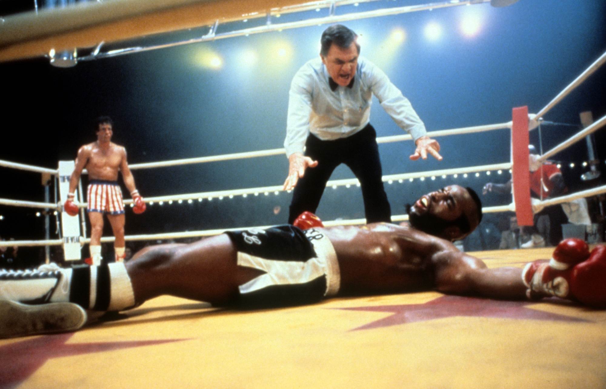 'Rocky III' movies Sylvester Stallone as Rocky and Carl Weathers as Apollo Creed. Rocky standing in the corner of the ring and Apollo on the ground with the referee counting.