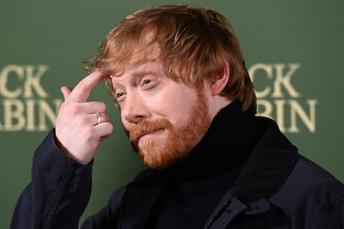 Rupert Grint smiles in front of a green background.