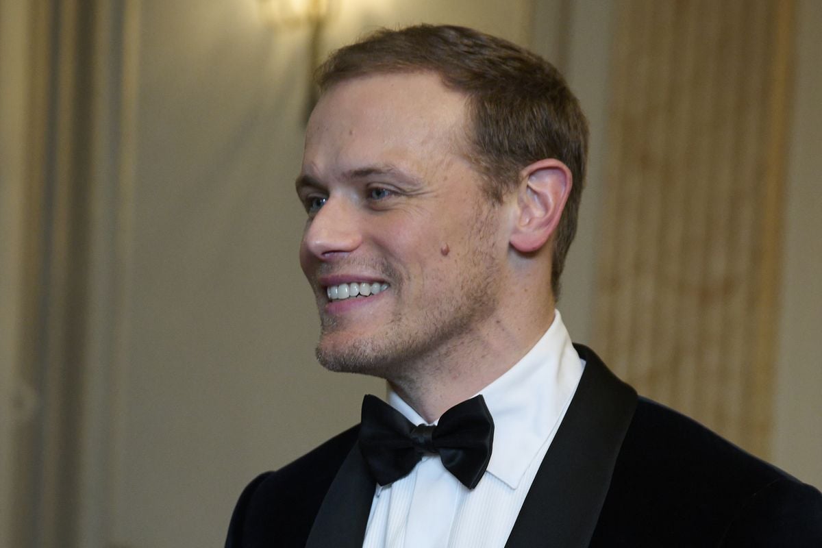Sam Heughan smiles while wearing a tuxedo.