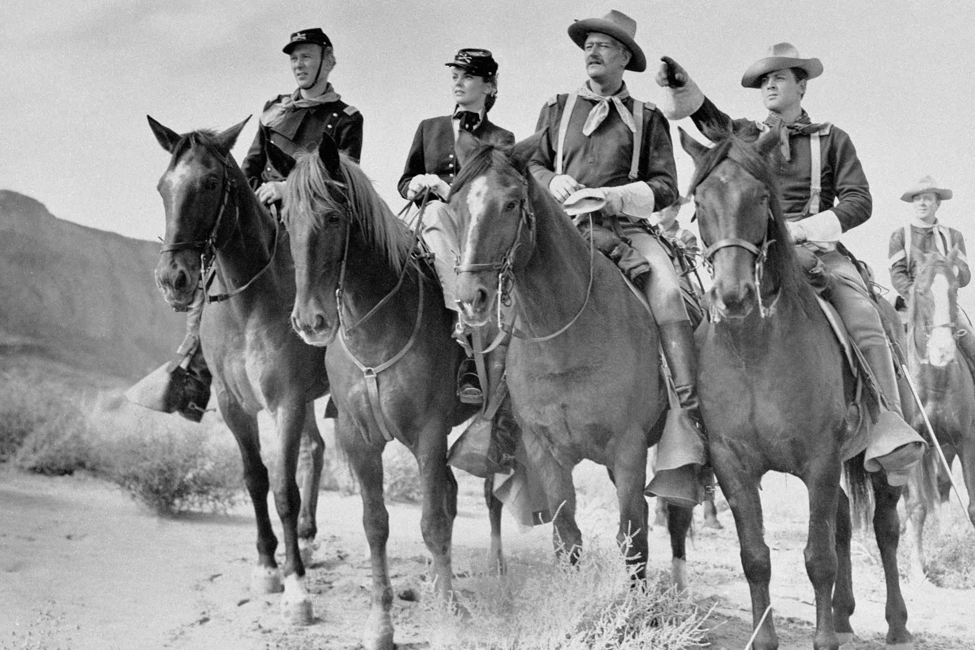 'She Wore a Yellow Ribbon' John Agar as Lt. Flint Cohill, Joanne Dru as Olivia Dandridge, John Wayne as Capt. Brittlese, and Ben Johnson as Sgt. Tyree riding their horses, looking ahead and pointing.