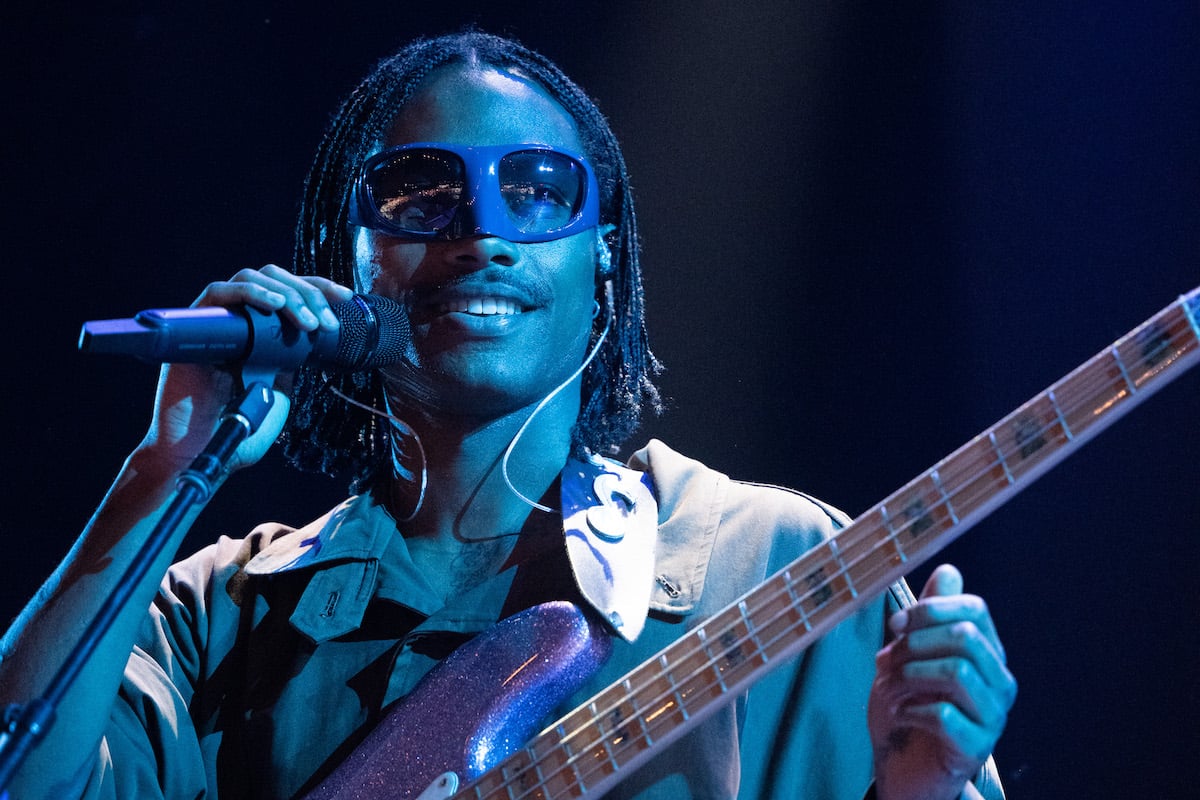 Steve Lacy holds a guitar and sings into a microphone on stage.