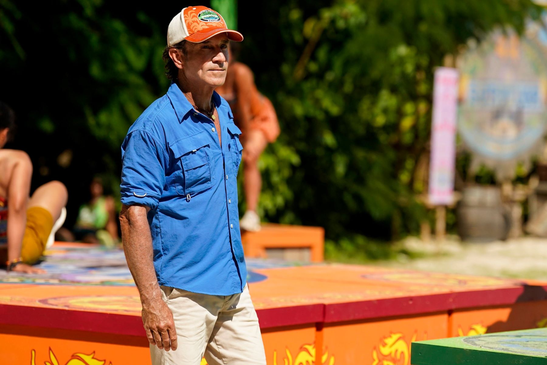 Jeff Probst, who hosts the 'Survivor 44' premiere, wears a blue button-up shirt with rolled-up sleeves, white shorts, and an orange and white 'Survivor' baseball cap.