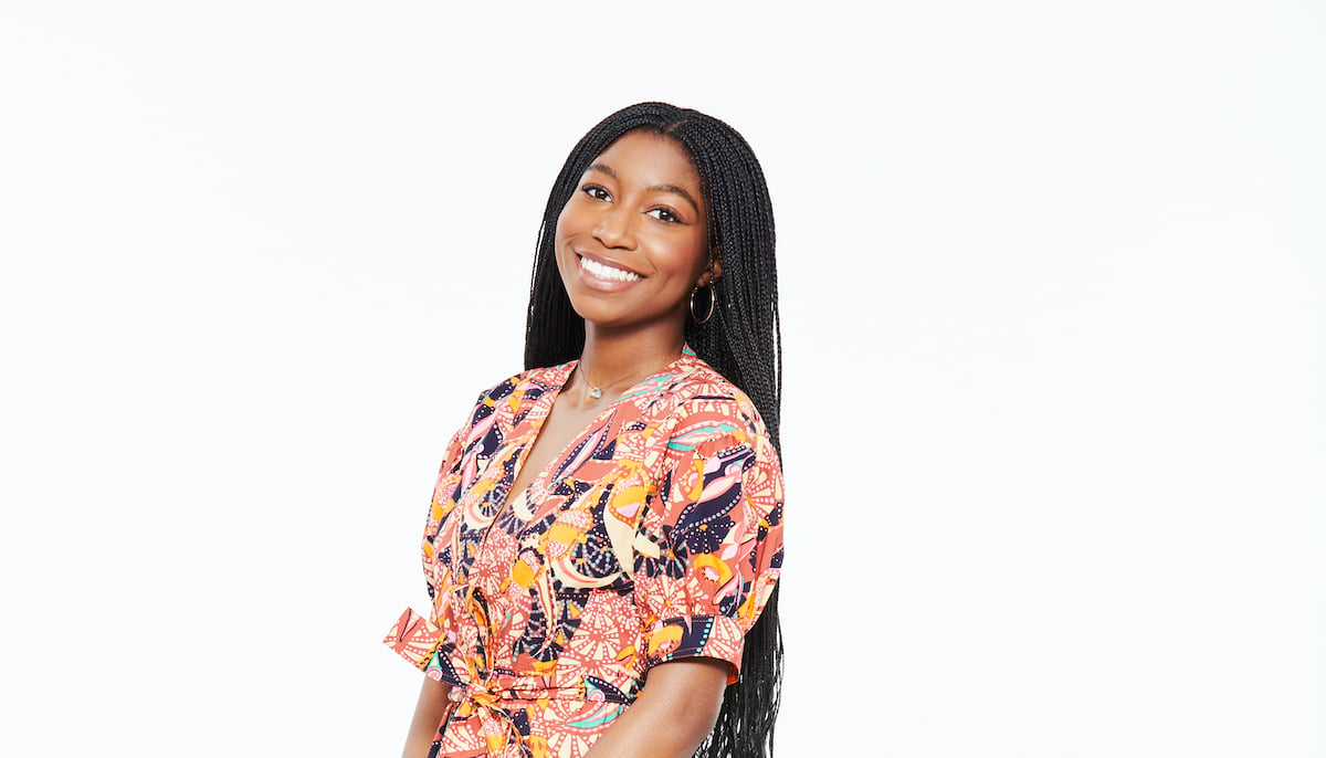 Tabyana Ali as Trina Robinson, smiling, standing in front of a white background