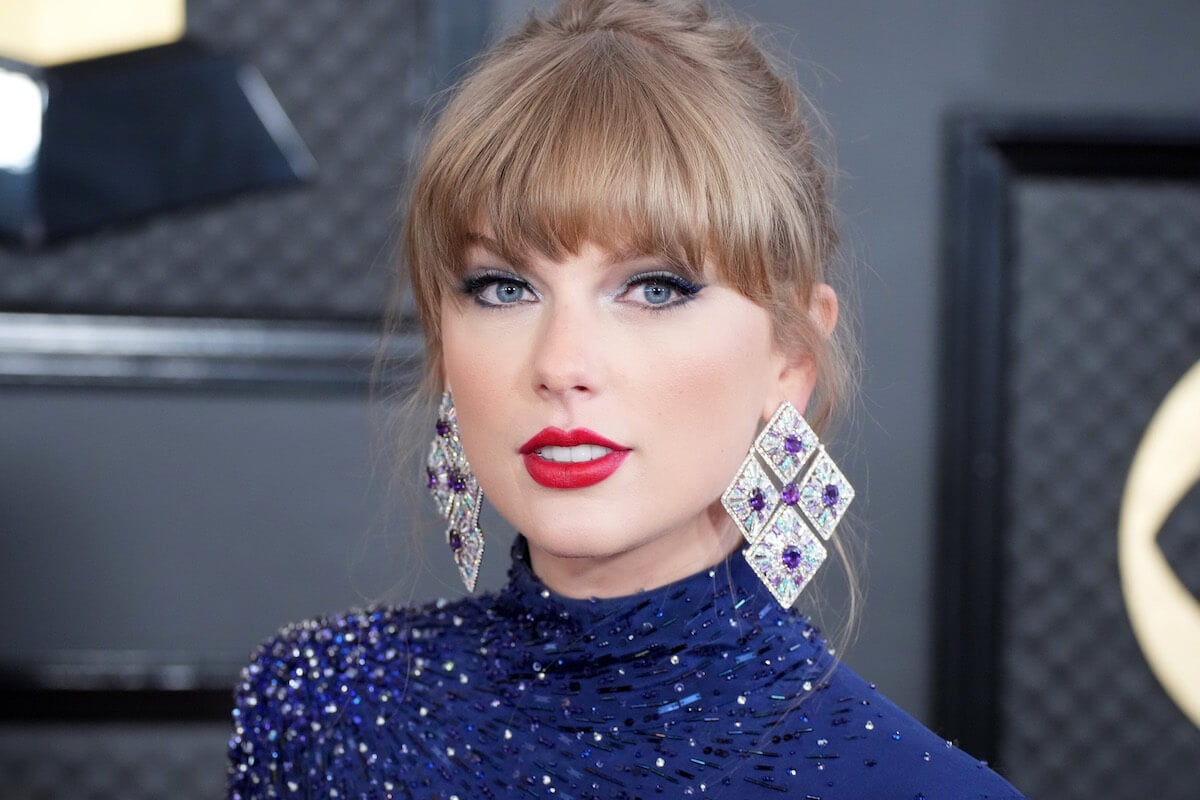 Singer Taylor Swift poses at an event wearing a sparkly blue top and silver and blue earrings.