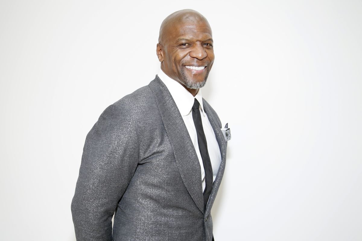 Terry Crews smiles while posing for photos against a white background.