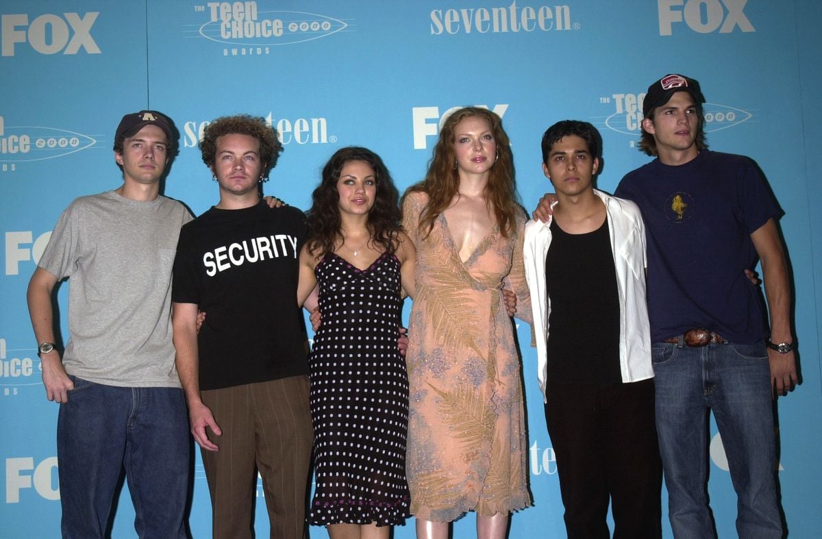 The cast of "That 70s Show" poses for a photo in front of a blue backdrop.