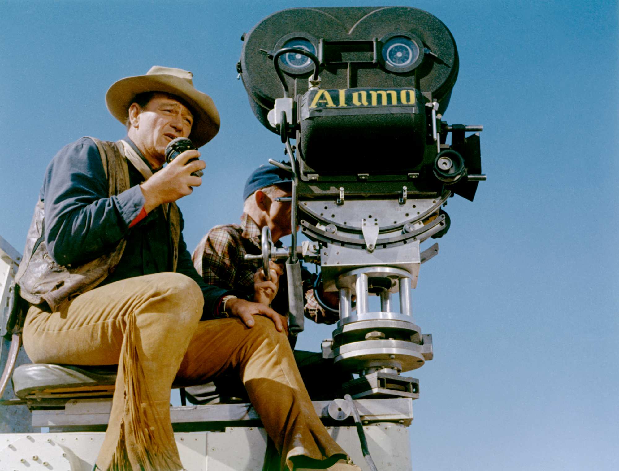 'The Alamo' director John Wayne sitting behind a movie camera wearing a Western movie costume