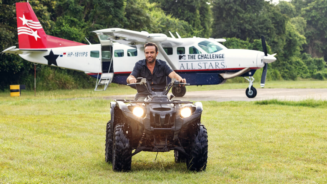 T.J. Lavin on an ATV in front of a helicopter with 'The Challenge: All Stars' logo
