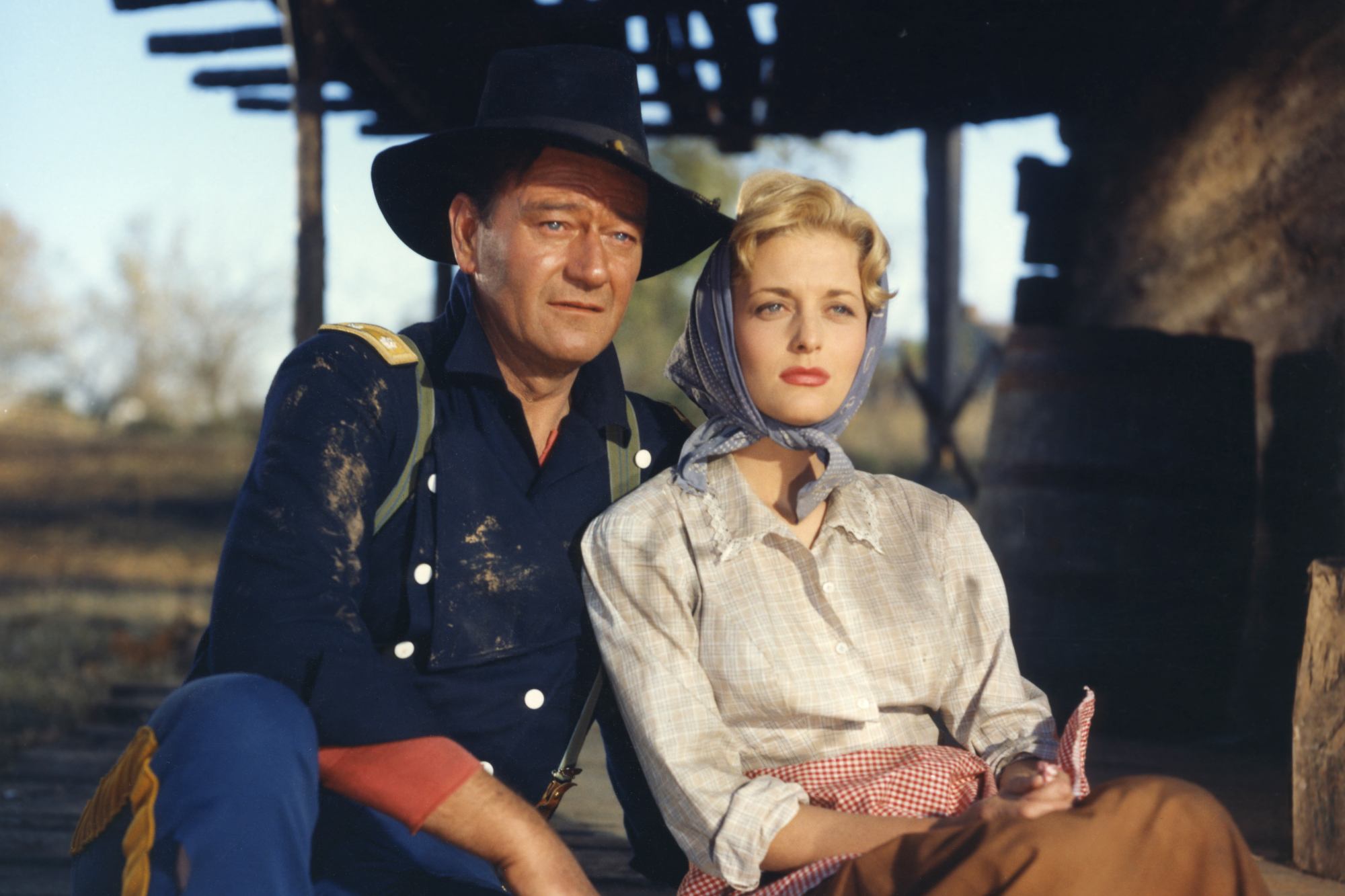 'The Horse Soldiers' John Wayne as Col. John Marlowe and Constance Towers as Hannah Hunter sitting next to each other, looking out with a house's overhang behind them.