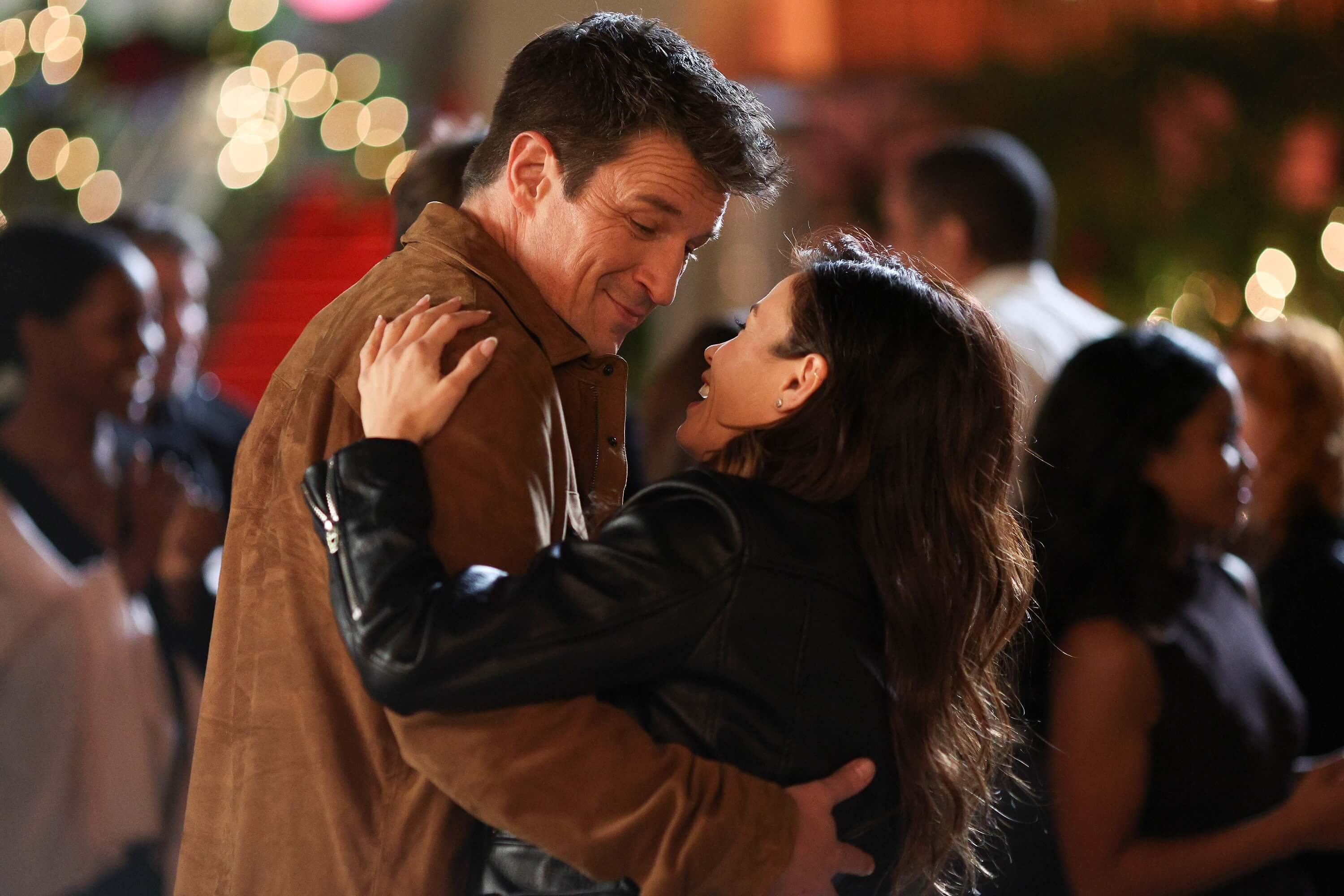 Nathan Fillion and Jenna Dewan star as John Nolan and Bailey Nune in 'The Rookie' Season 5. They share a scene where they are dancing. Nolan wears a light brown jacket. Bailey wears a black leather jacket.