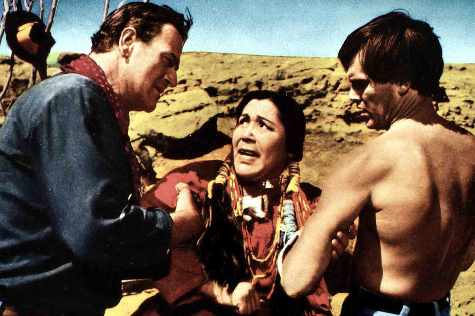 'The Searchers' John Wayne as Ethan Edwards, Beulah Archuletta as Look, and Jeffrey Hunter as Martin Pawley. Wayne is gripping ARchuletta's arm, while she holds onto Pawley's arm.