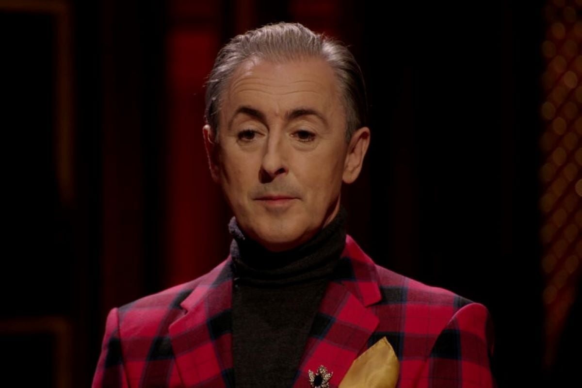 Alan Cumming, the host of 'The Traitors,' which will have a reunion that airs on Peacock, wears a red and black plaid suit over a black turtleneck.