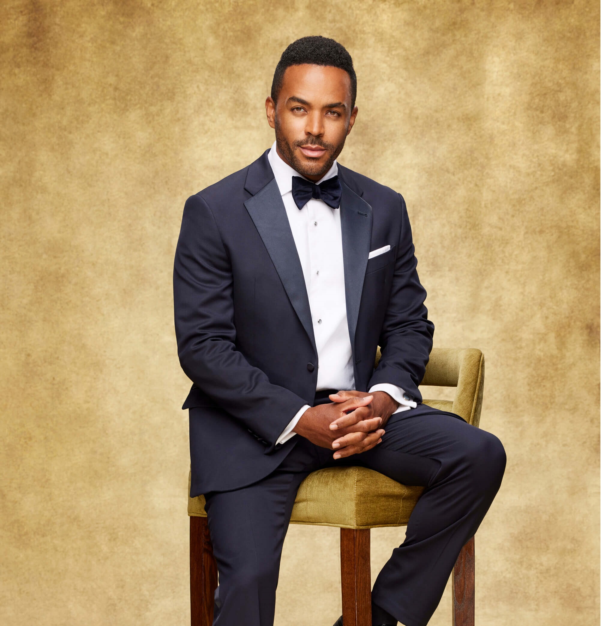 'The Young and the Restless' star Sean Dominic dressed in a blue suit; sits on a stool while posing for a photo.