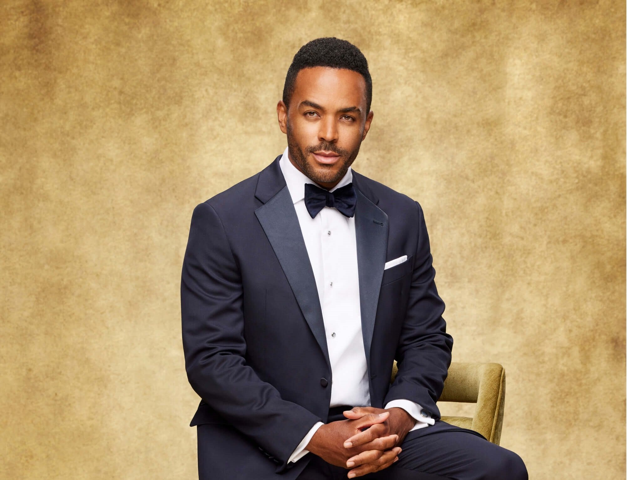 'The Young and the Restless' star Sean Dominic dressed in a blue suit; sits on a stool while posing for a photo.