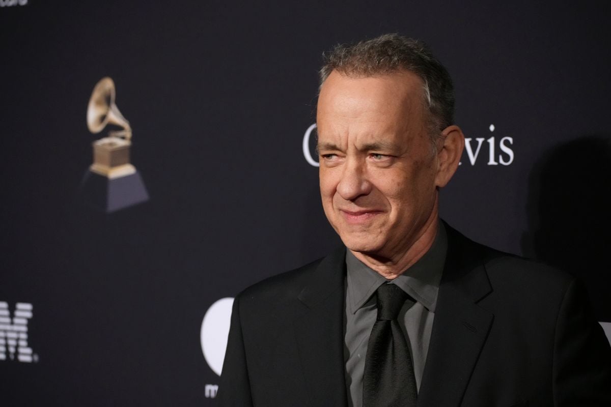Tom Hanks poses for photos in front of a black backdrop with the Grammys logo