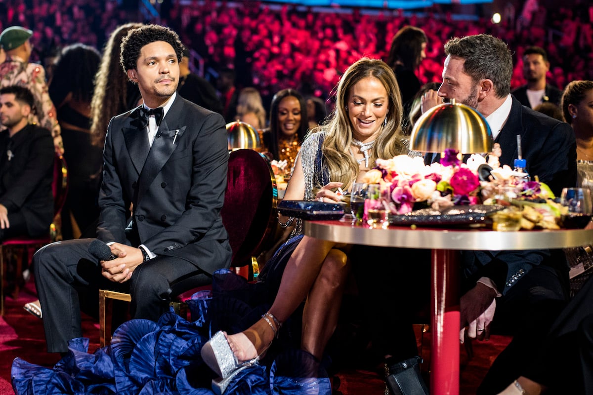 Trevor Noah sitting in chair next to Jennifer Lopez and Ben Affleck as they speak to each other at the 65th annual Grammy Awards.