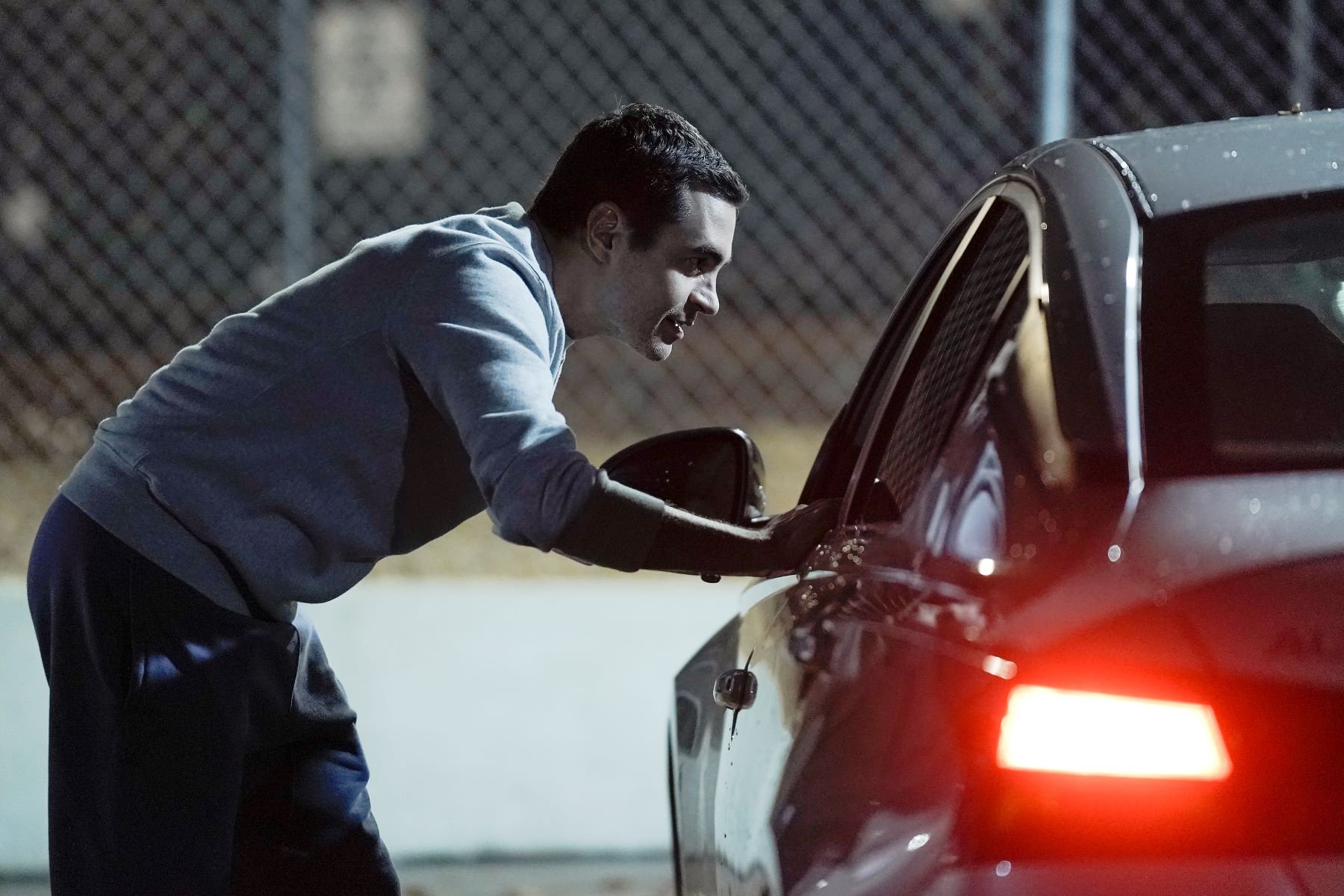 Ramón Rodríguez, in character as Will Trent in 'Will Trent' Season 1 Episode 6, wears a light gray sweater and blue sweatpants as he approaches a car.
