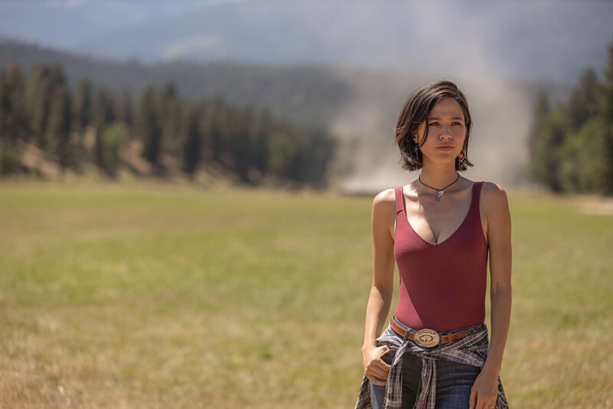 In Yellowstone, Monica stands on the Dutton family ranch wearing a red tank top and jeans.