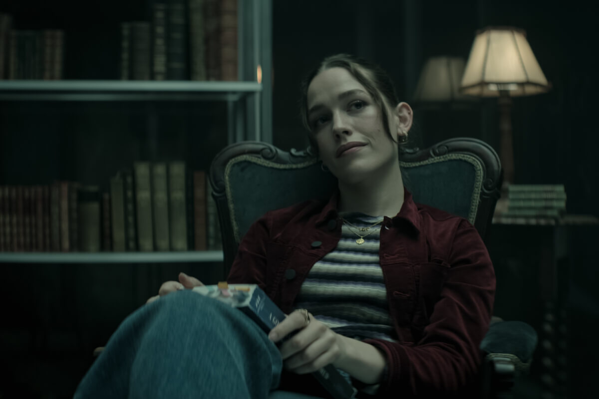 In the You Season 4 Part 2 trailer, Love Quinn sits in a chair wearing a striped top and maroon jacket.