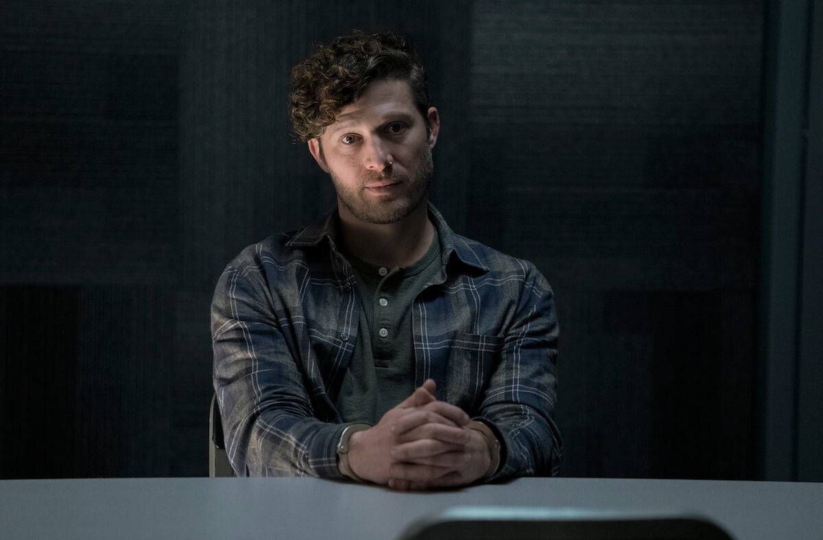 Zach Gilford as Elias Voit seated at a table in 'Criminal Minds: Evolution.' The character will return for season 2.